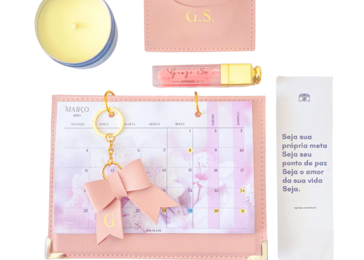 Foto de um kit rosa com calendário de mesa, chaveiro de laço, vela aromática, um gloss e um porta cartões representando um lindo presente para o dia internacional da mulher.
