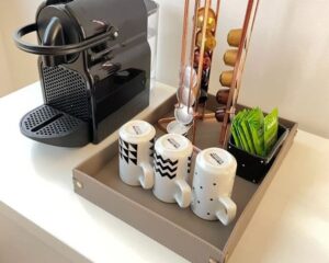 Foto de um aparador com cafeteira e xícaras em cima no cantinho do café.